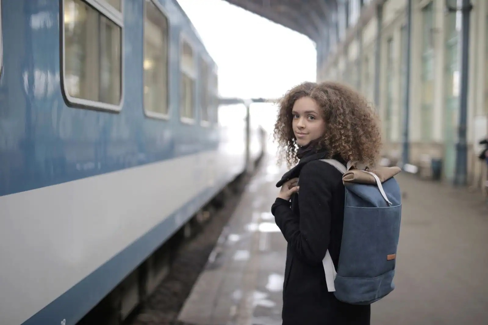 Jeune voyageuse avec un sac à dos sur le quai d'une gare, le long d'un train bleu