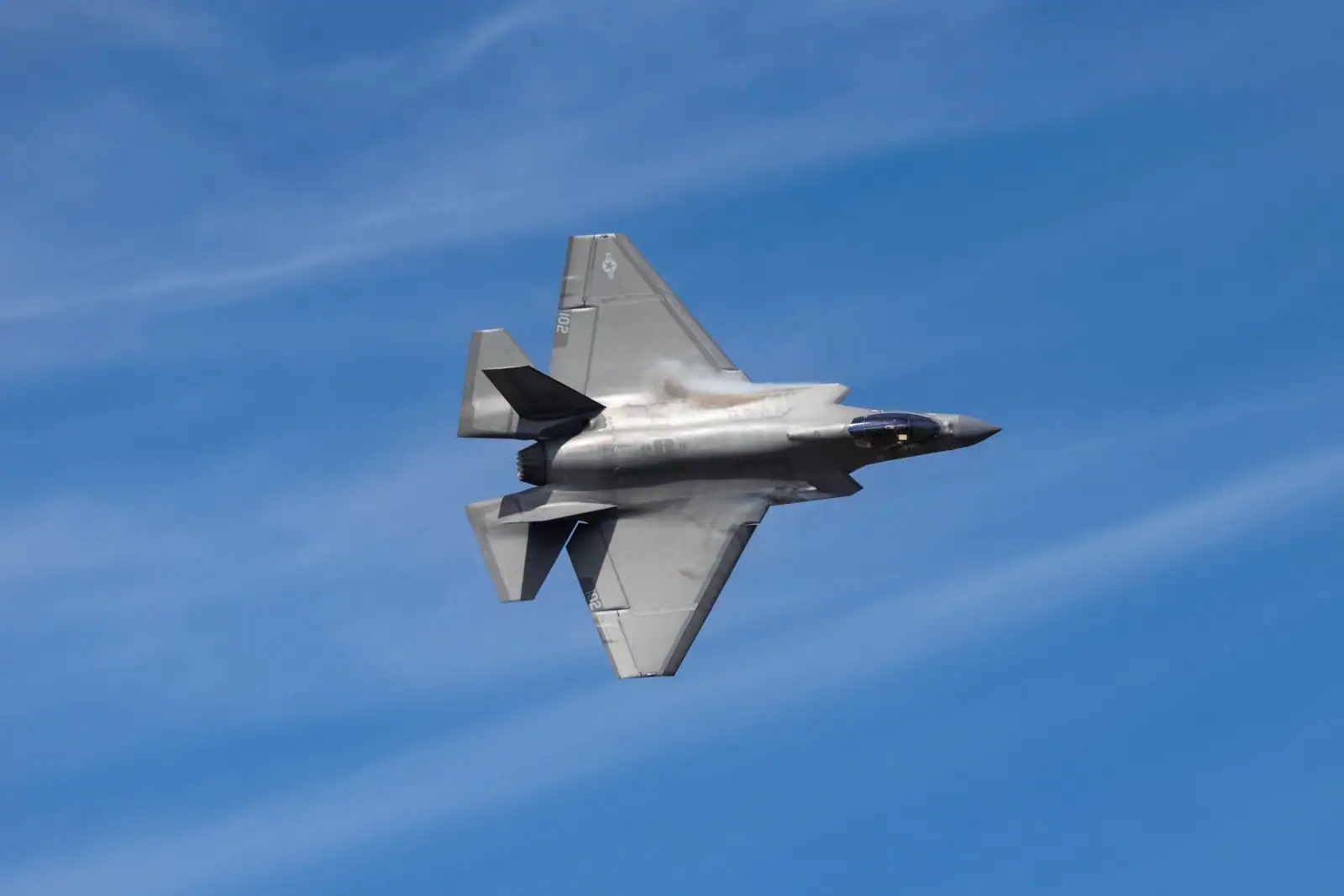 Chasseur furtif F-35 aux lignes anguleuses en vol sous un ciel bleu, vu de dessous.