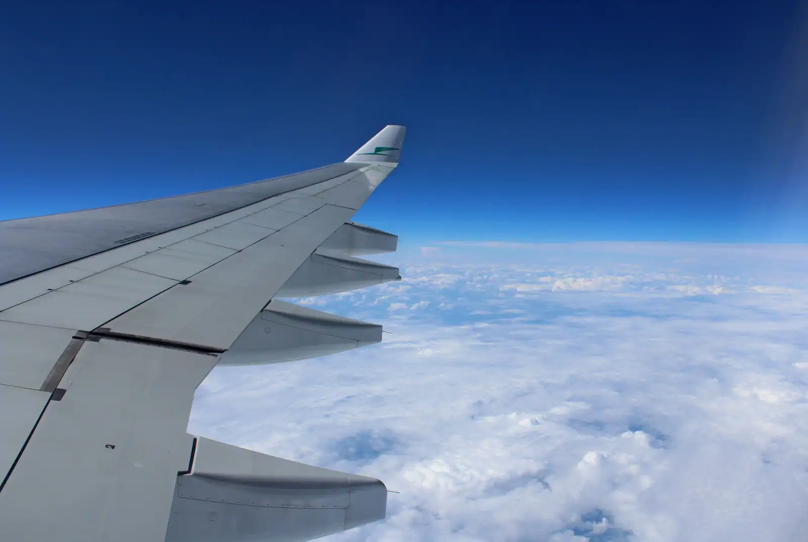 Aile d'un avion de ligne en vol au-dessus d'une mer de nuages, sous un ciel bleu dégagé