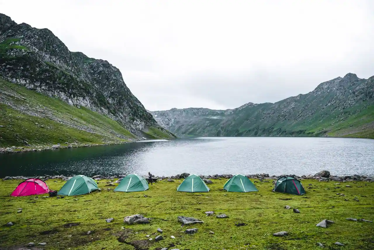 Tente de camping installée au bord d'un lac de montagne, avec des sommets en arrière-plan