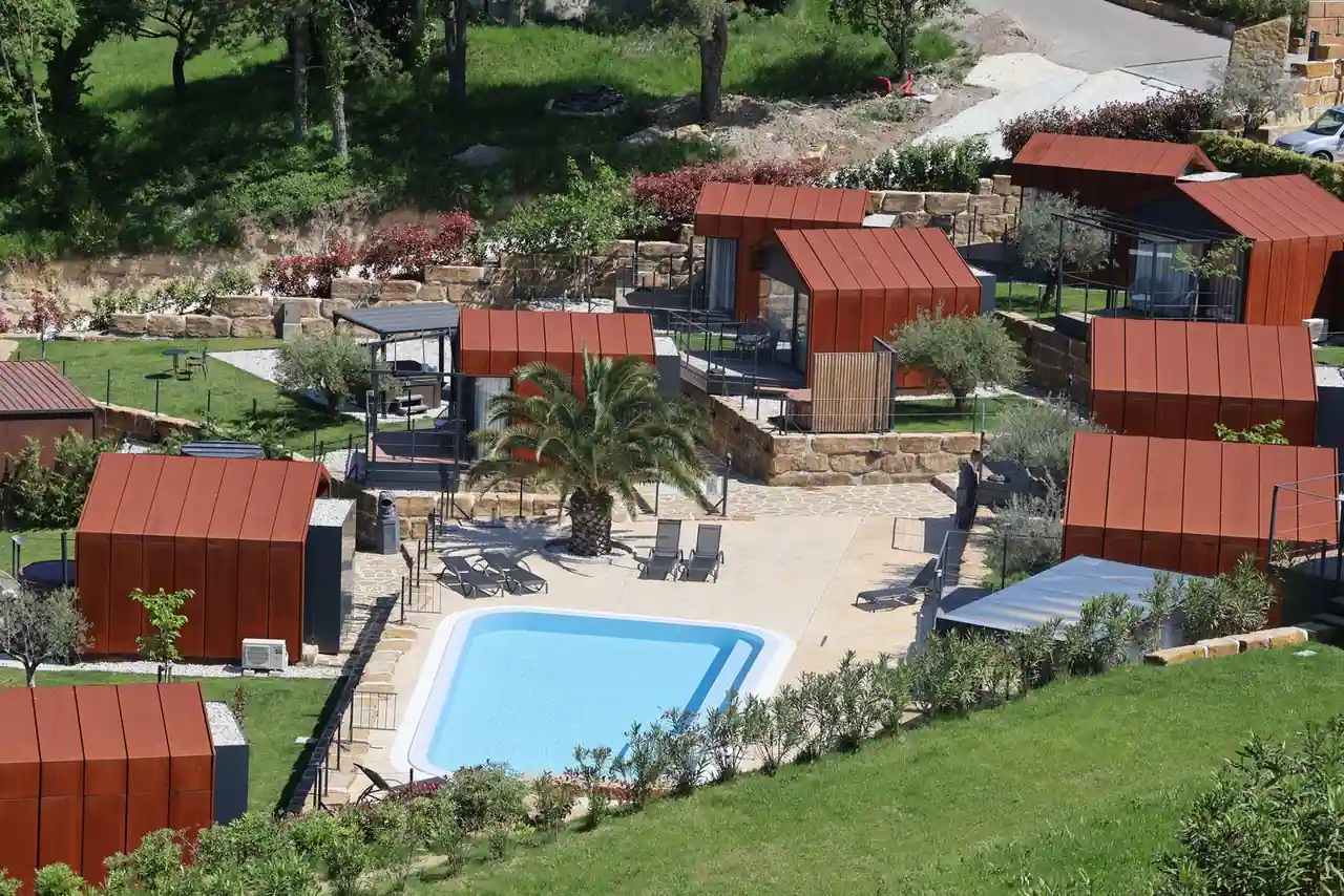 Camping haut de gamme avec piscine et chalets en bois entourés de verdure sous le soleil