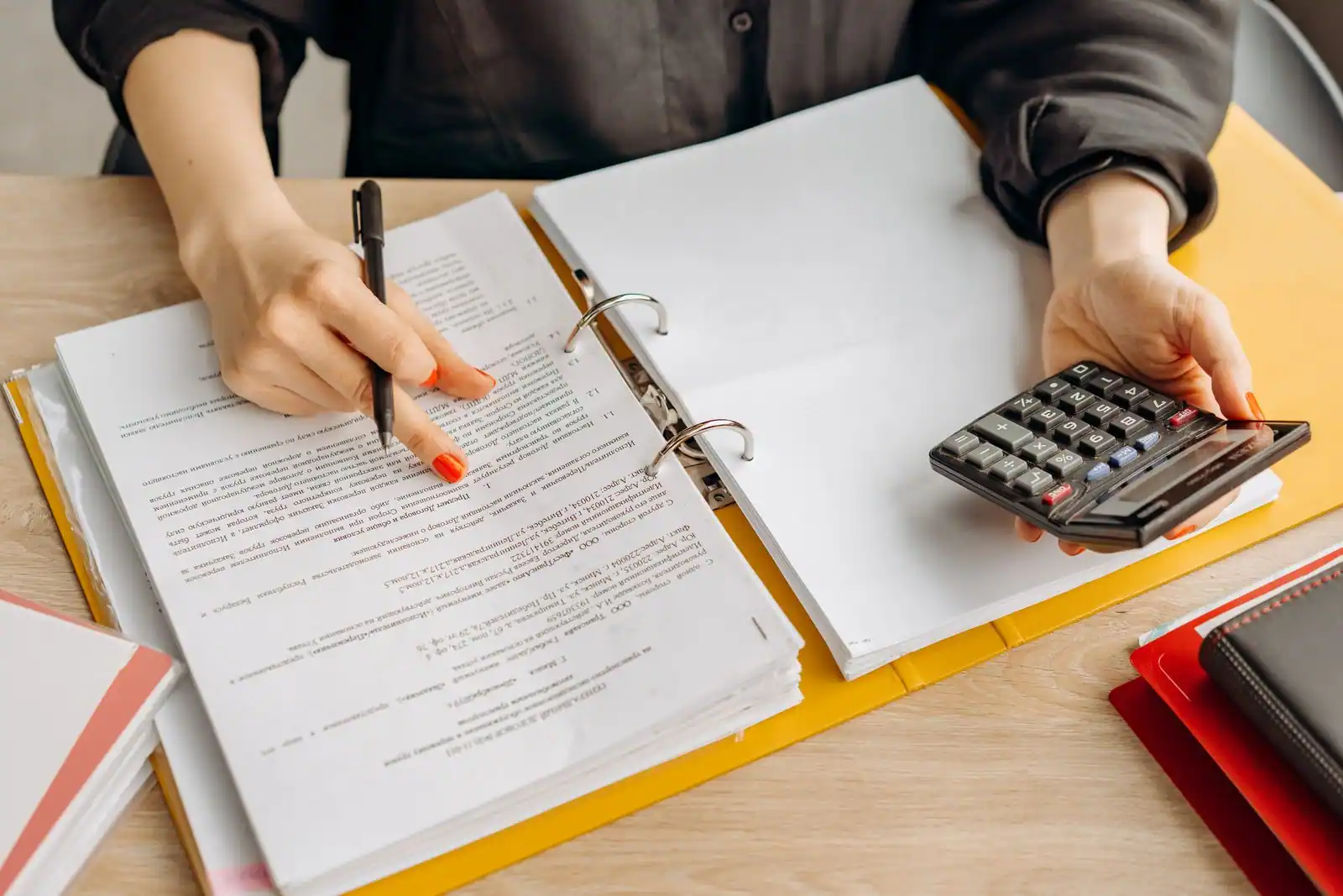 Personne examinant des documents avec un stylo et une calculatrice pour comparer des devis