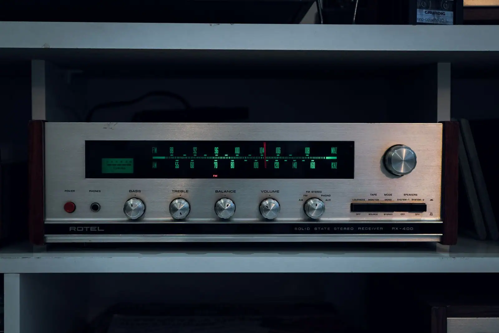 Ancien tuner radio hi-fi posé sur une étagère, son cadran de fréquences éclairé dans la pénombre