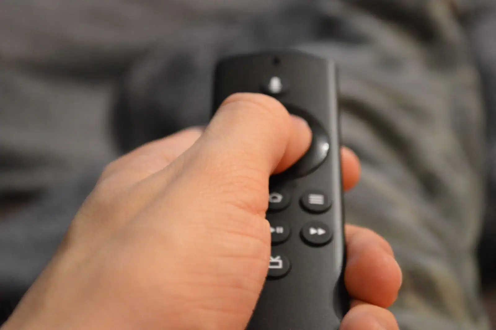 Main tenant une télécommande de télévision en gros plan, devant un canapé en arrière-plan flou.