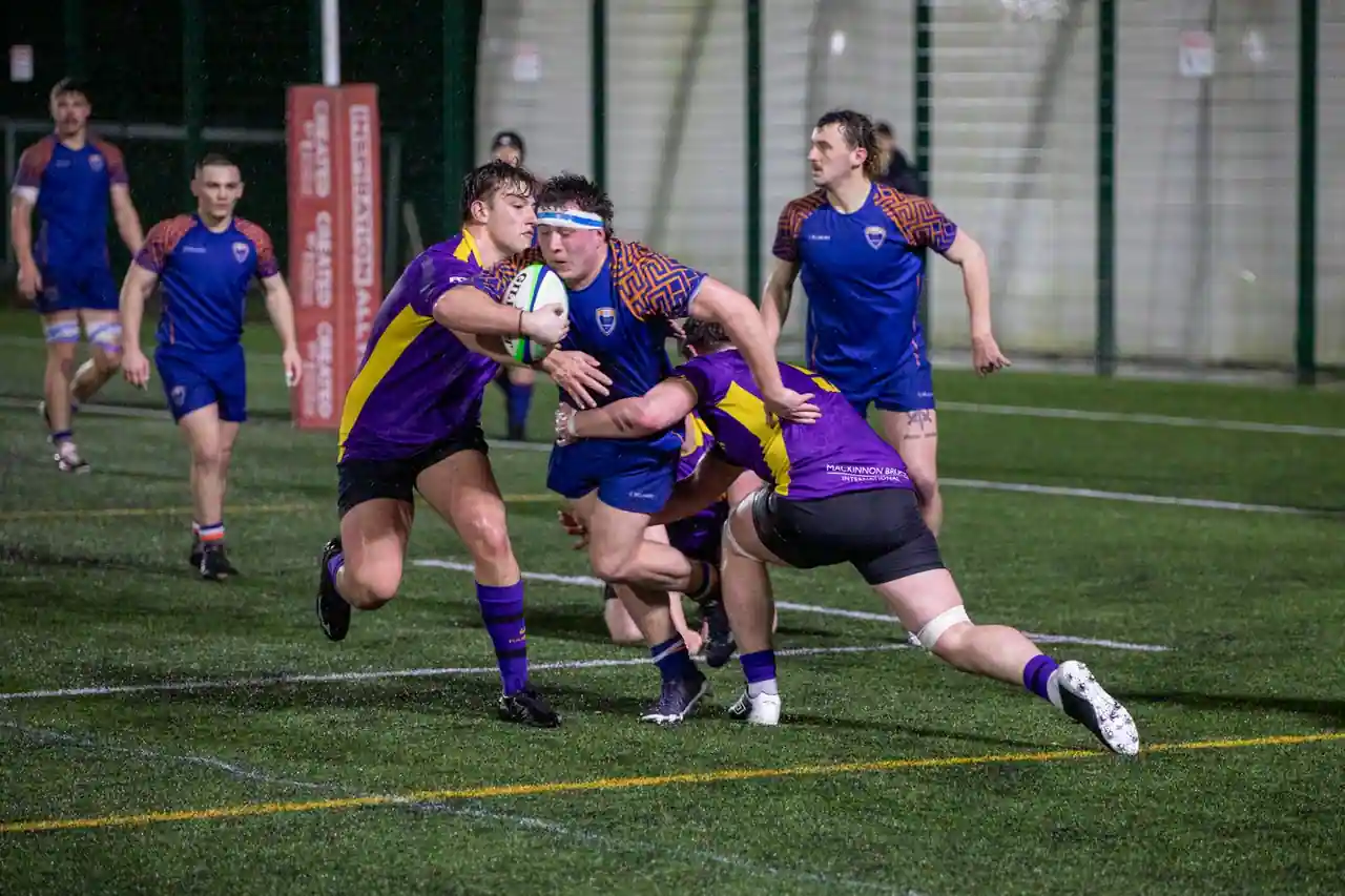 Joueurs de rugby à XV se disputant le ballon lors d'un match, sur un terrain éclairé