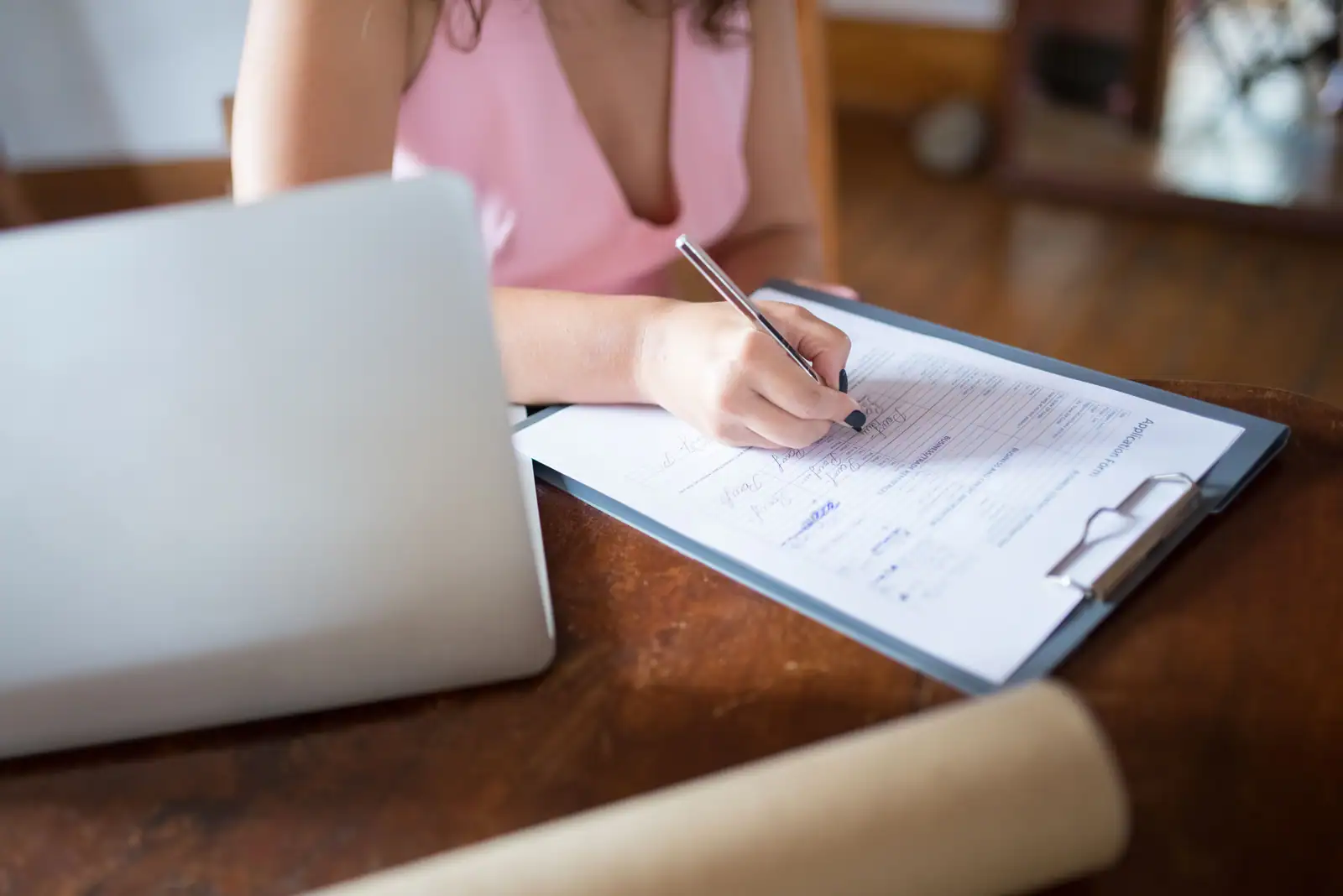 Personne remplissant un formulaire administratif à côté d'un ordinateur portable