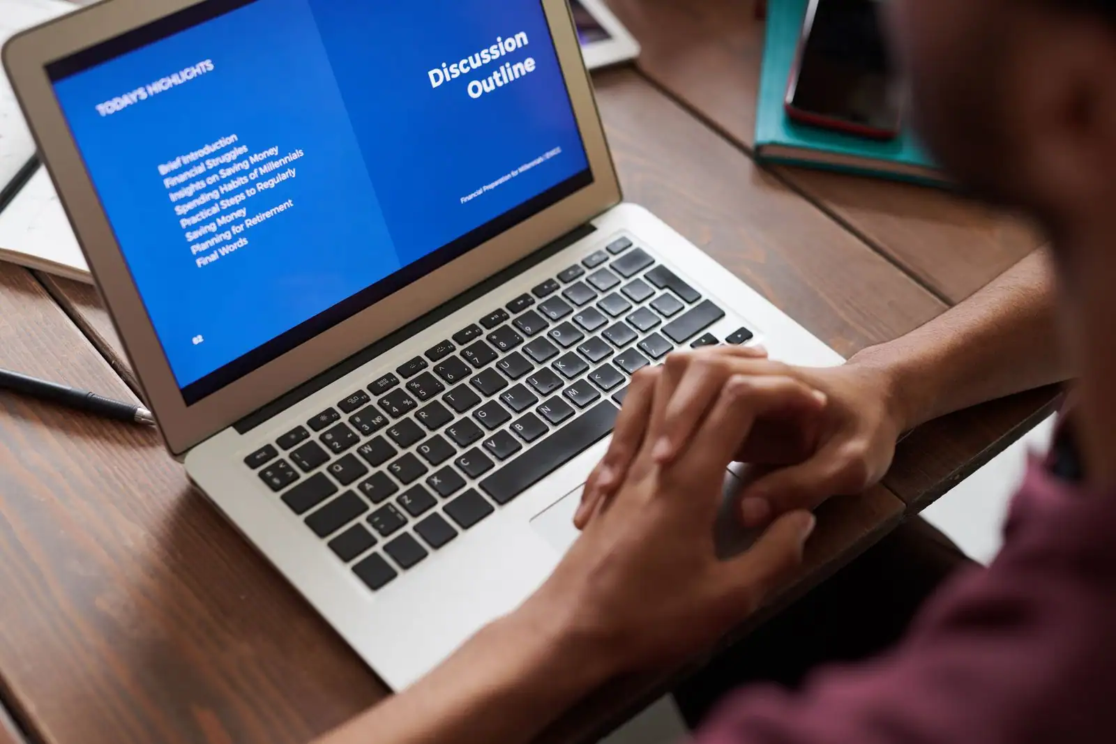 Une personne utilise un ordinateur portable posé sur un bureau, les mains sur le clavier et l'écran allumé.