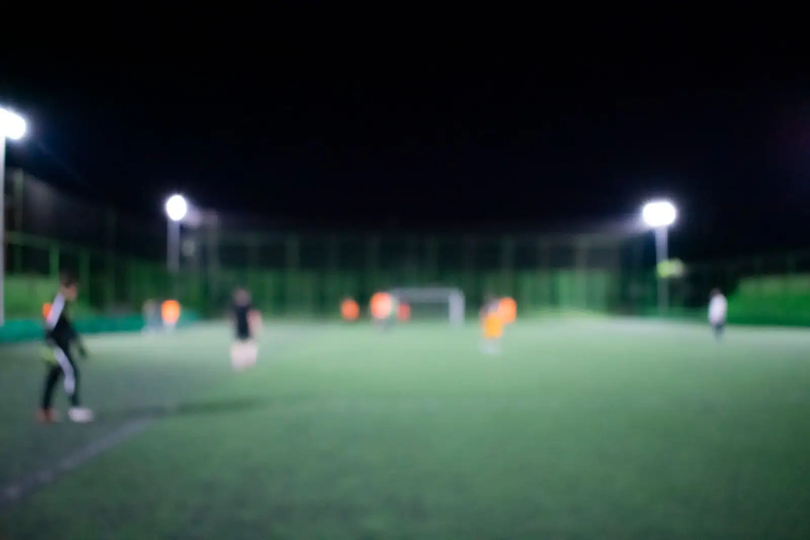 Joueurs de football sur un terrain en gazon éclairé par des projecteurs en soirée.