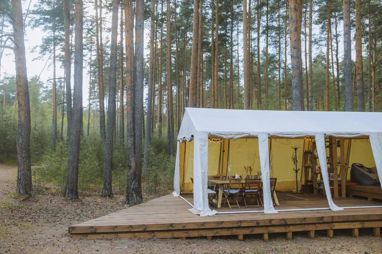 Tente de glamping confortable et meublée installée en pleine nature, avec une terrasse en bois