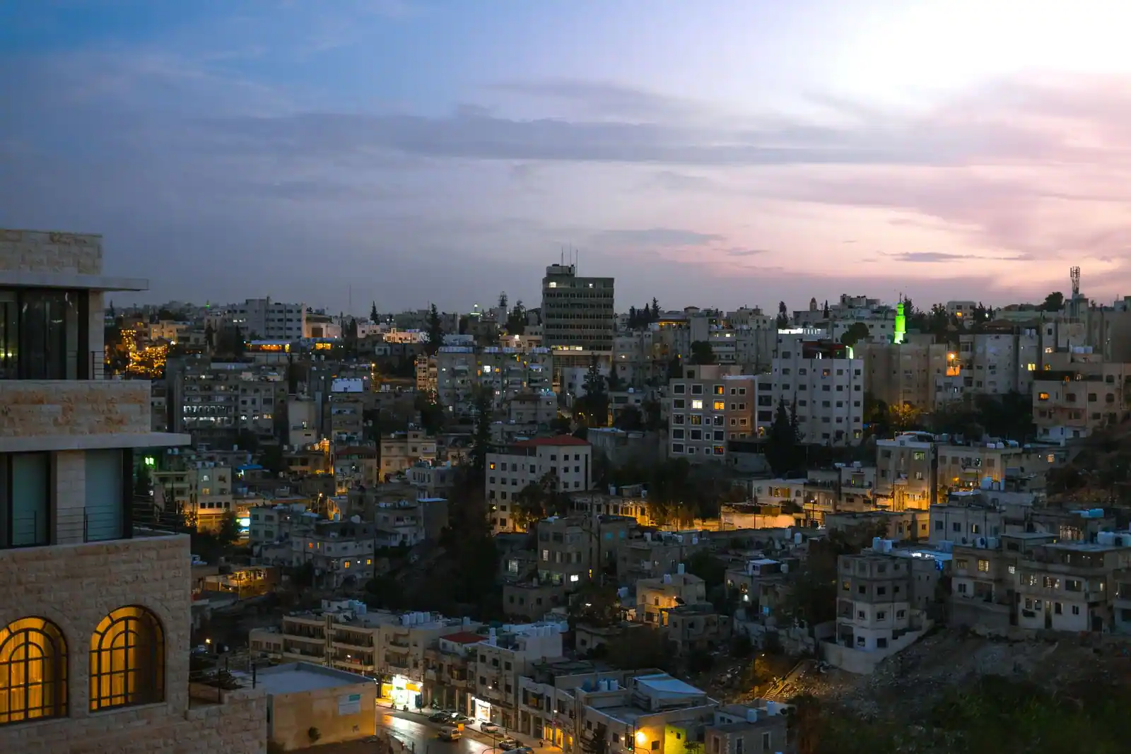Vue d'une ville du Moyen-Orient au crépuscule, quartiers résidentiels en pente éclairés sous un ciel rosé.