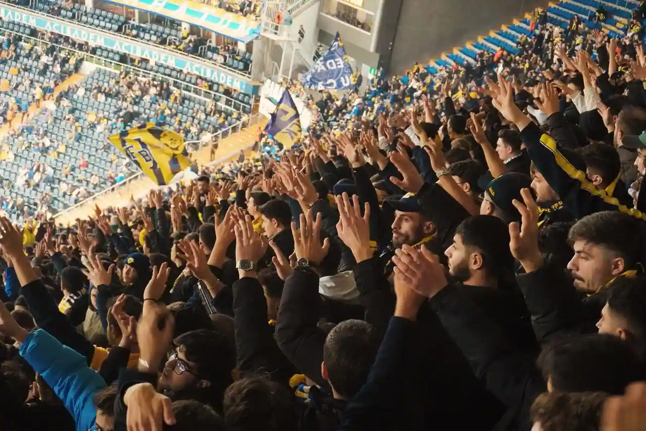 Ambiance de stade pendant un match de football, tribunes remplies de supporters.