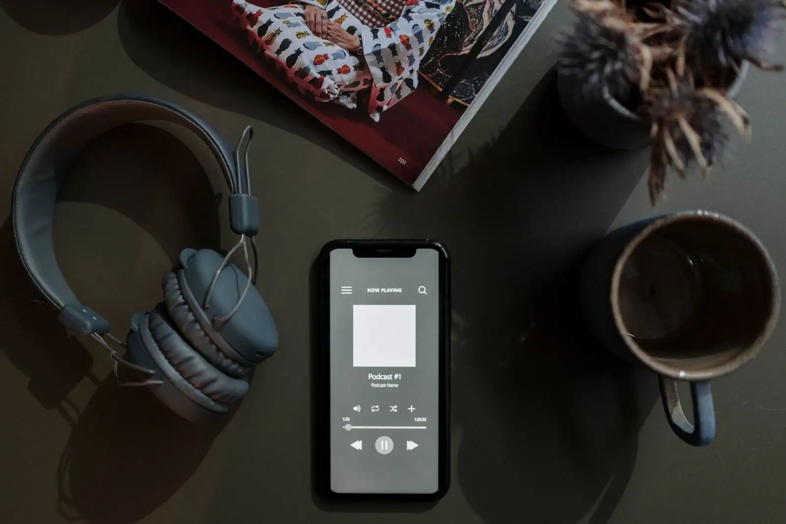 Smartphone affichant une application de podcast, posé près d'un casque audio et d'une tasse.