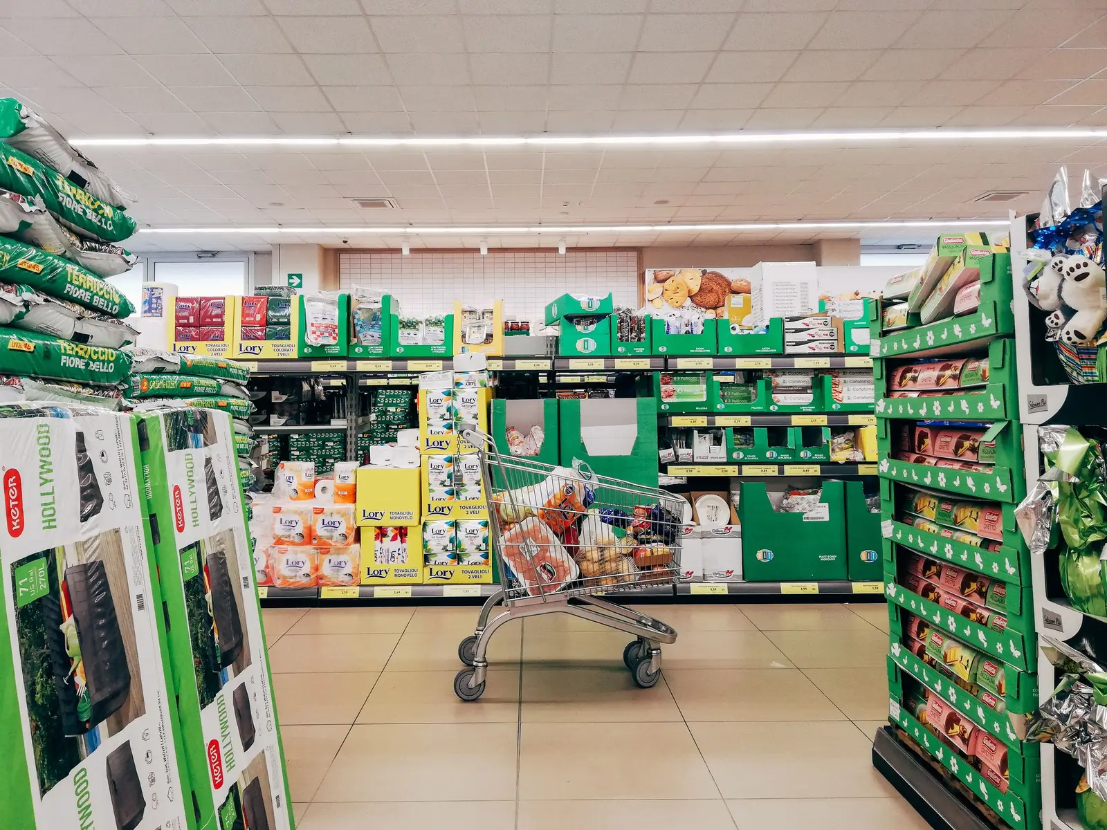 Chariot de courses rempli dans une allée de supermarché, devant des rayons de produits