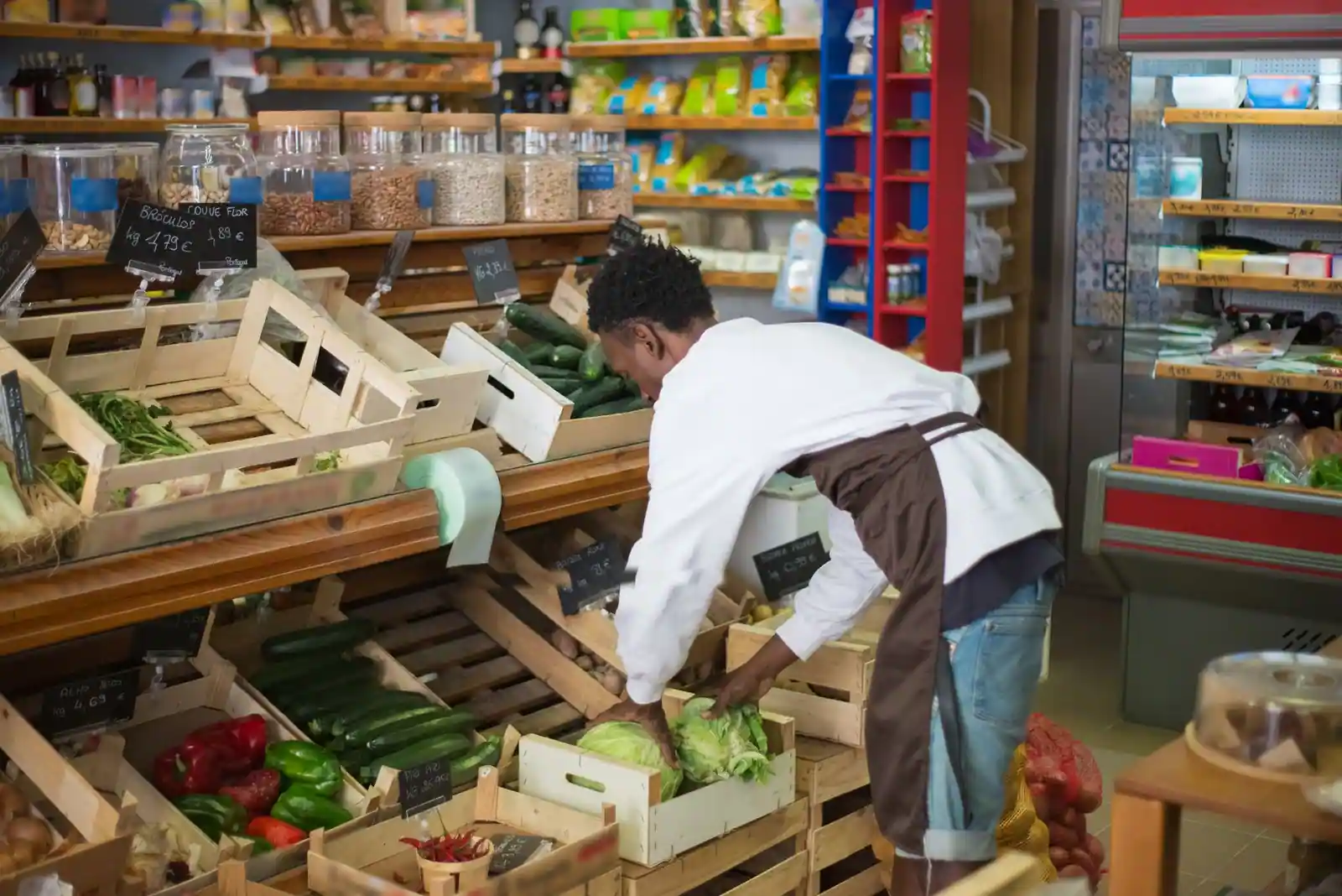 Employé d'un commerce de primeurs disposant des légumes frais dans des cagettes en bois.