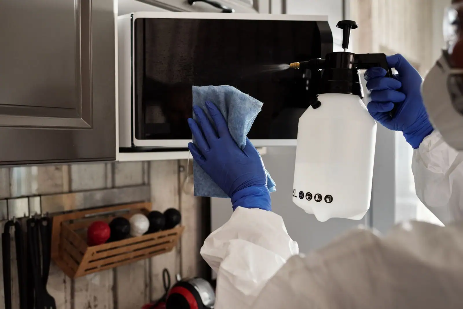 Personne en gants nettoyant une cuisine à l'aide d'un vaporisateur et d'un chiffon en microfibre.