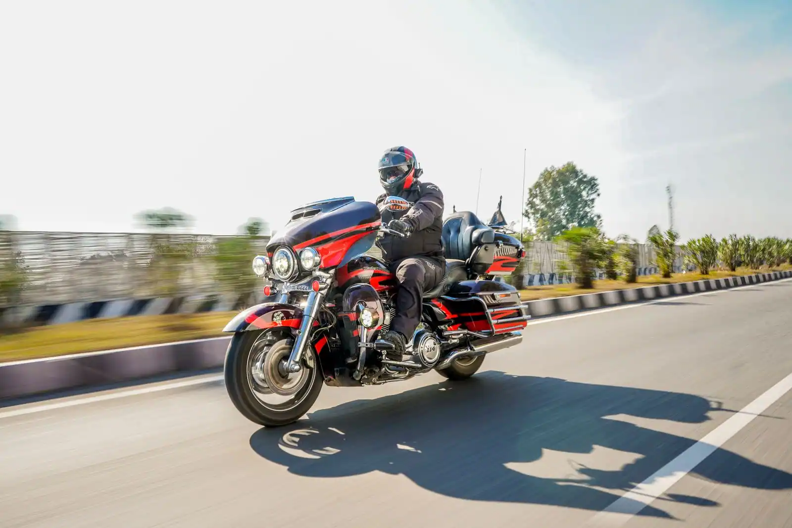 Motard en tenue et casque roulant sur une route dégagée en pleine journée, sur une moto de tourisme.