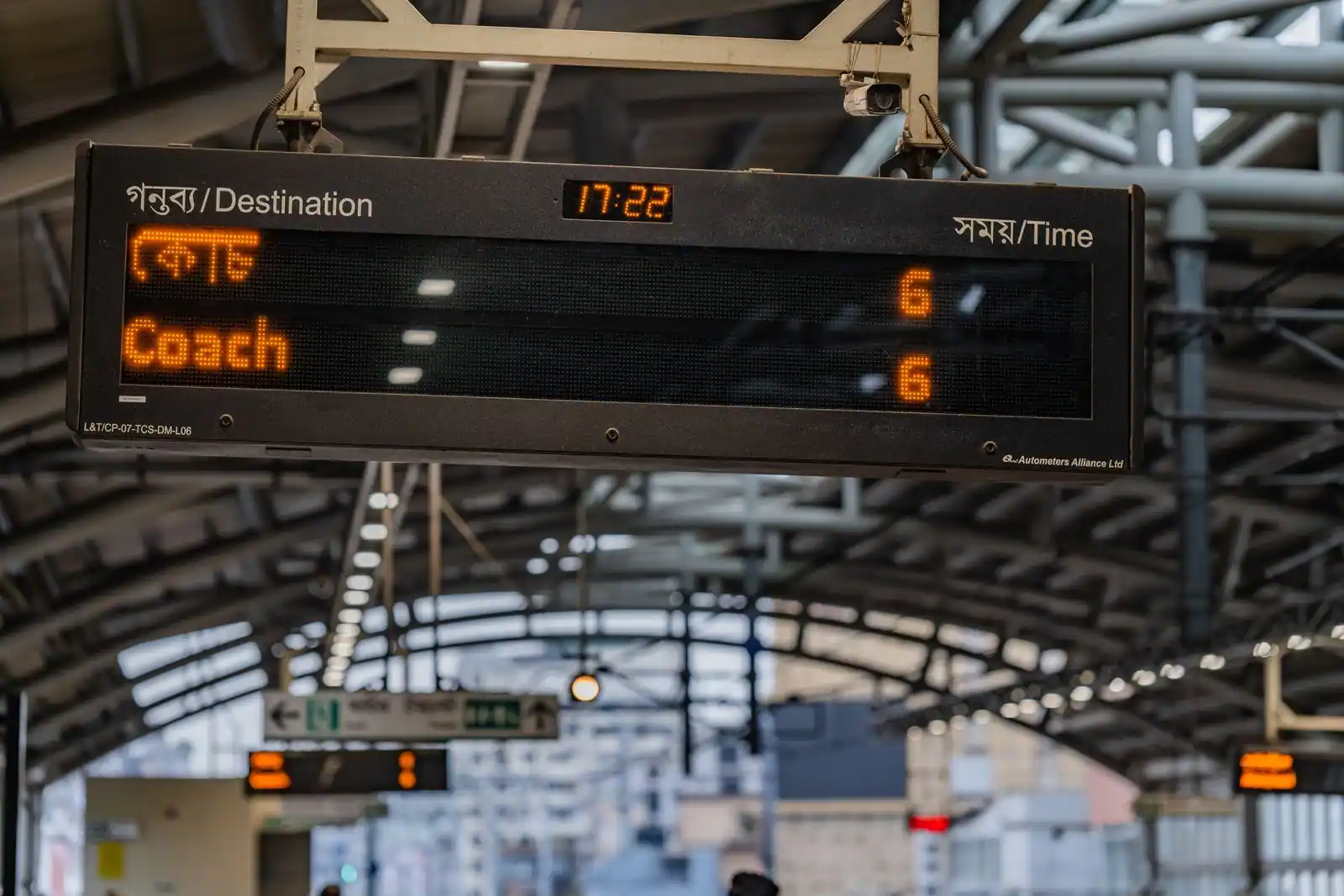 Tableau d'affichage numérique des trains, indiquant destination et horaire, sous la verrière d'une gare.