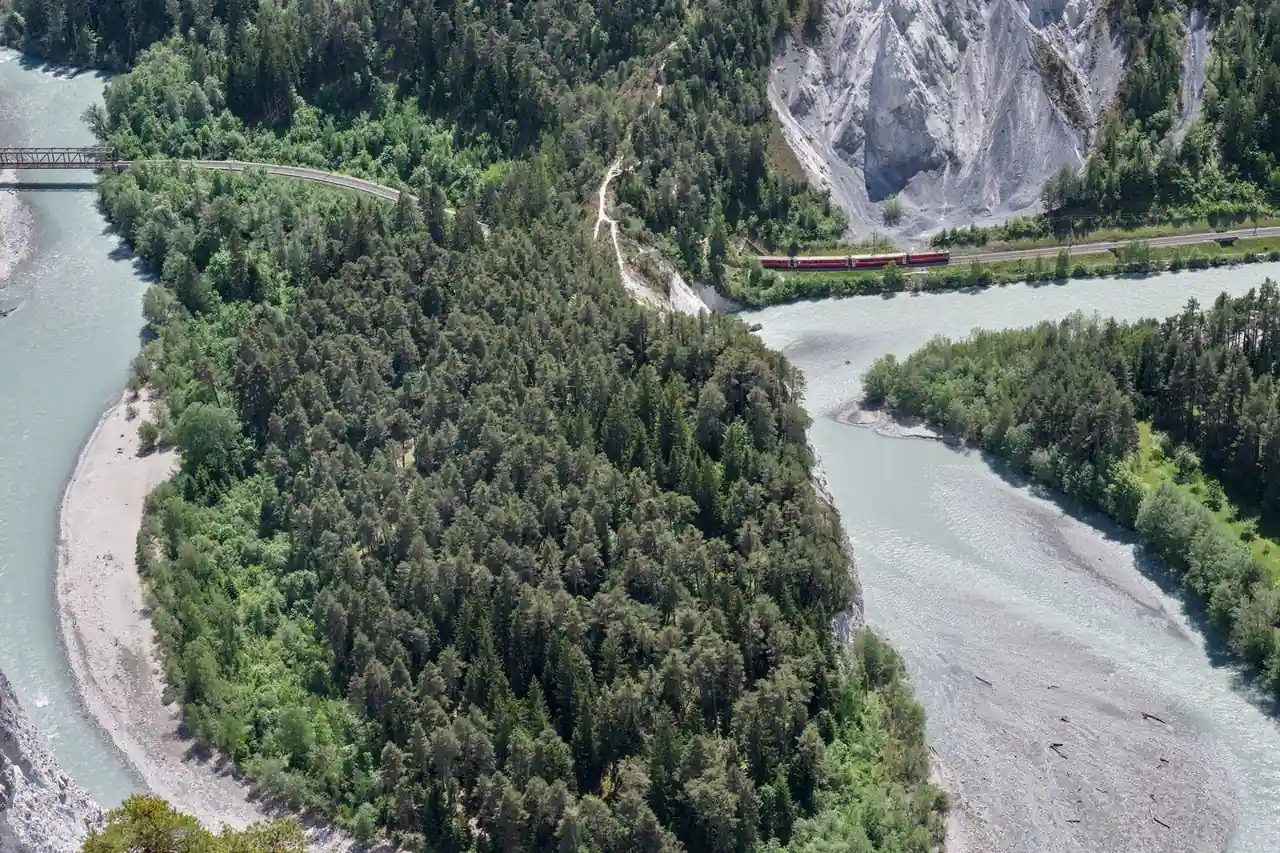 Petit train régional traversant un paysage de montagne boisée en été