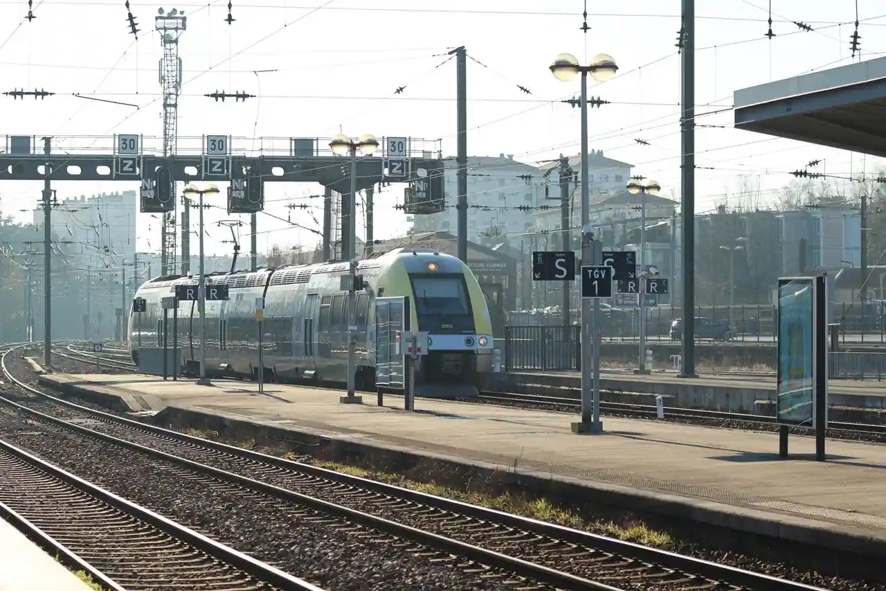 Train de voyageurs à quai le long des voies, dans une gare française ensoleillée.