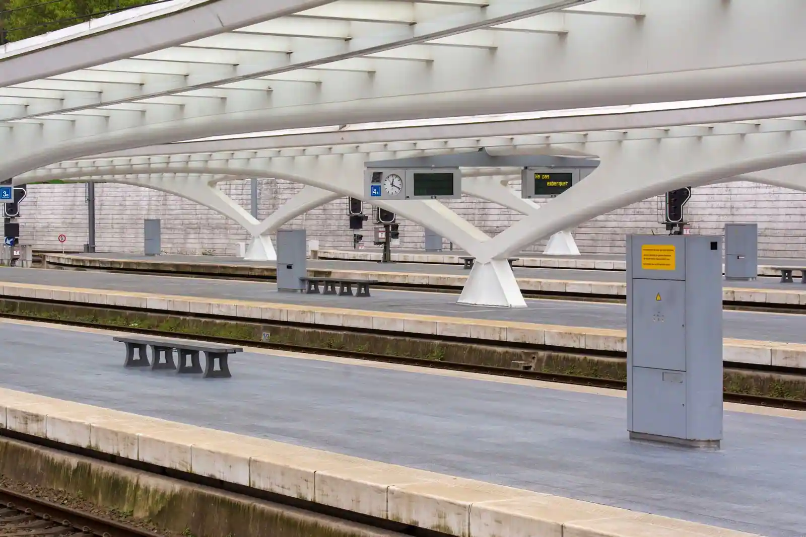 Quais déserts et voies d'une gare ferroviaire abritée par une grande verrière claire.
