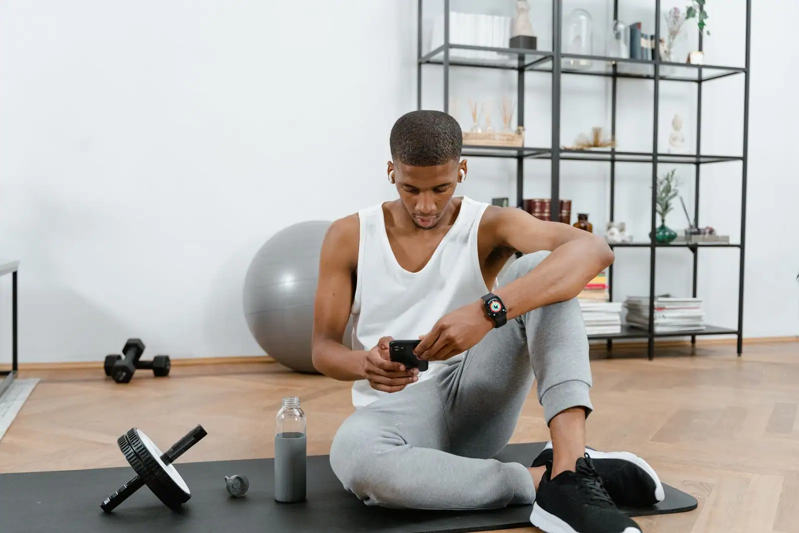 Sportif consultant son smartphone sur un tapis de fitness, entouré d'haltères et d'une bouteille d'eau