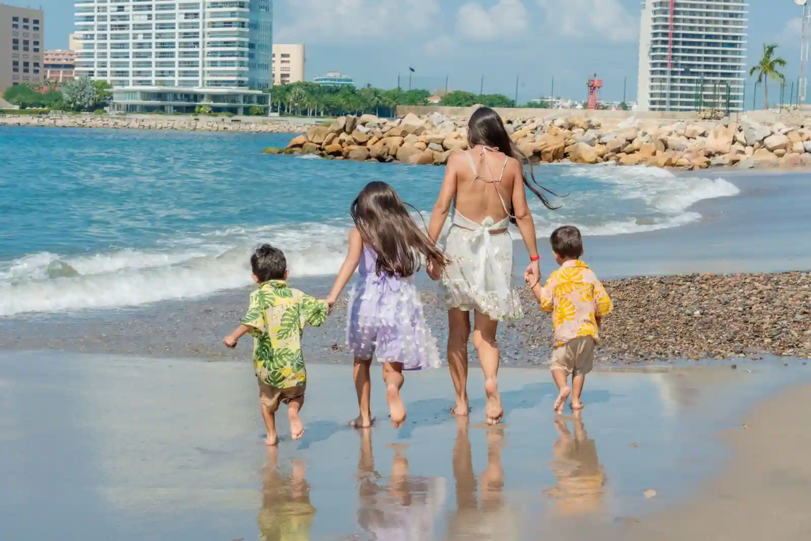 Un adulte et trois enfants marchant main dans la main au bord de l'eau sur une plage