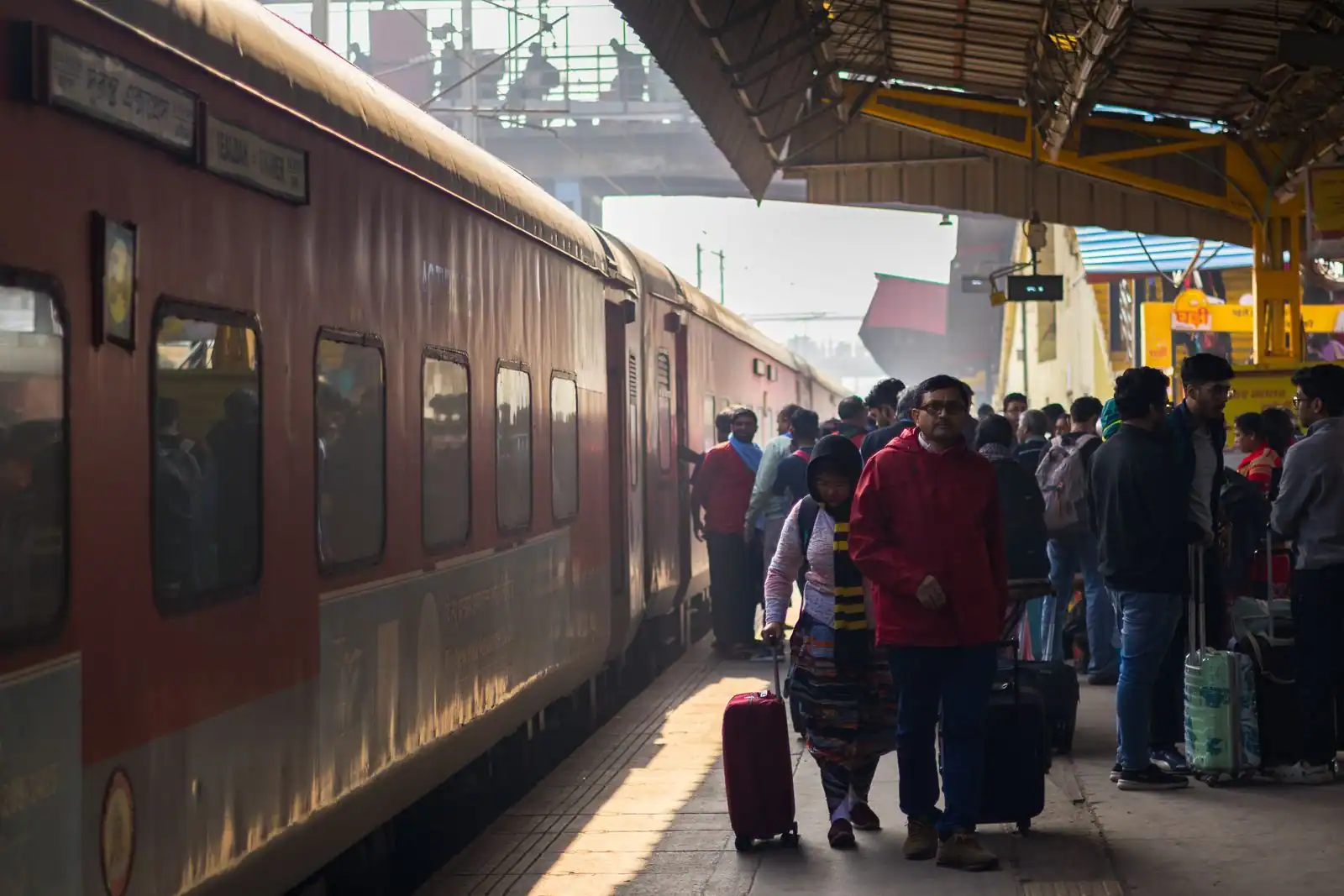 Des voyageurs avec leurs bagages s'apprêtent à monter à bord d'un train, le long du quai d'une gare.