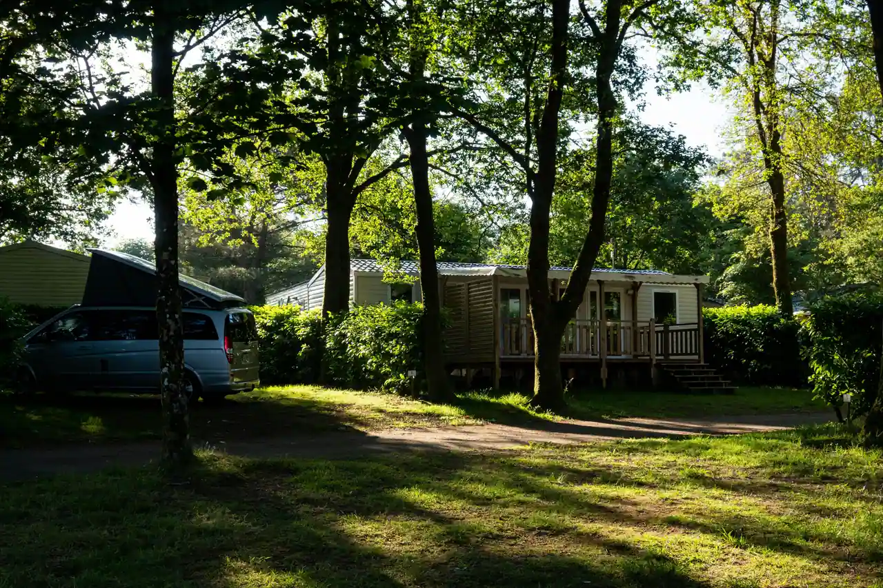 Mobil-home avec terrasse en bois et van aménagé sur des emplacements de camping ombragés