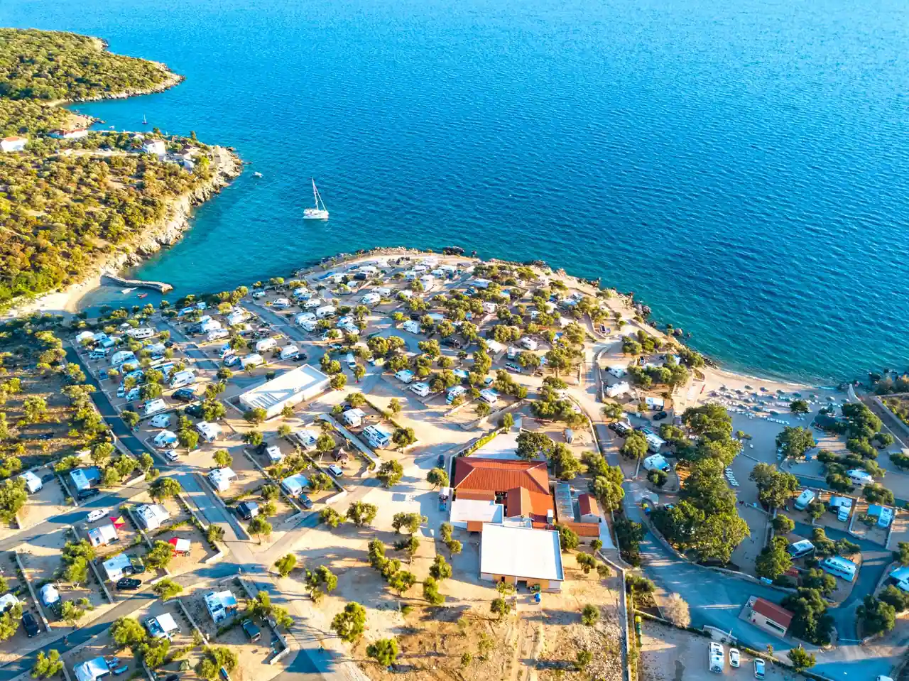 Vue aérienne d'un camping en bord de mer, emplacements et mobil-homes alignés le long du littoral.