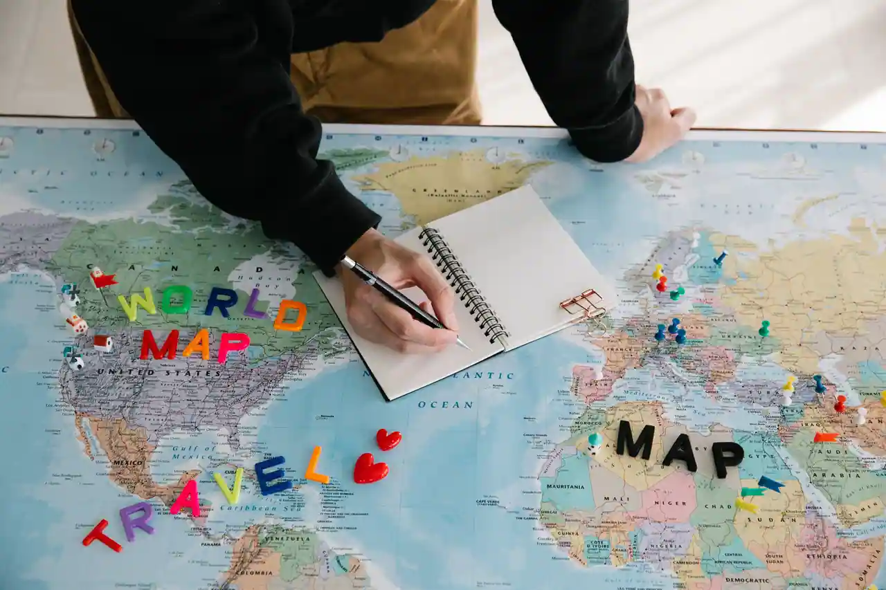 Planification d'un voyage : carnet ouvert et punaises de couleur posés sur une carte du monde