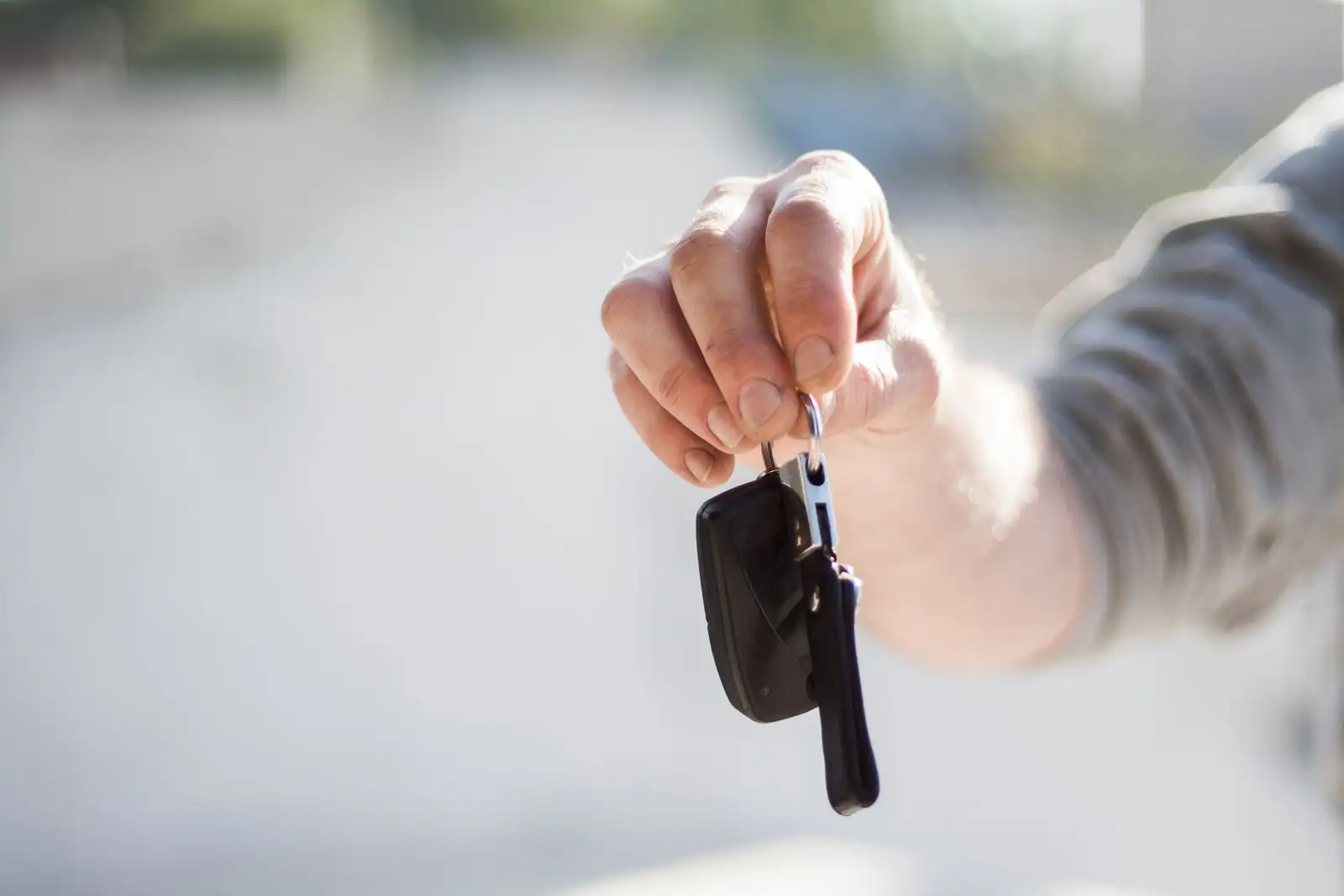 Main tendue présentant une clé de voiture avec télécommande, en extérieur sur fond clair