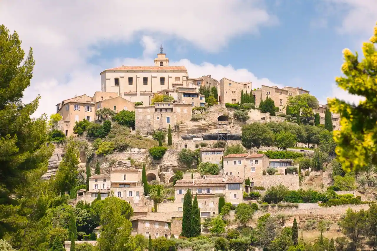 Village perché aux maisons de pierre claire adossé à une colline, entouré de cyprès et de verdure