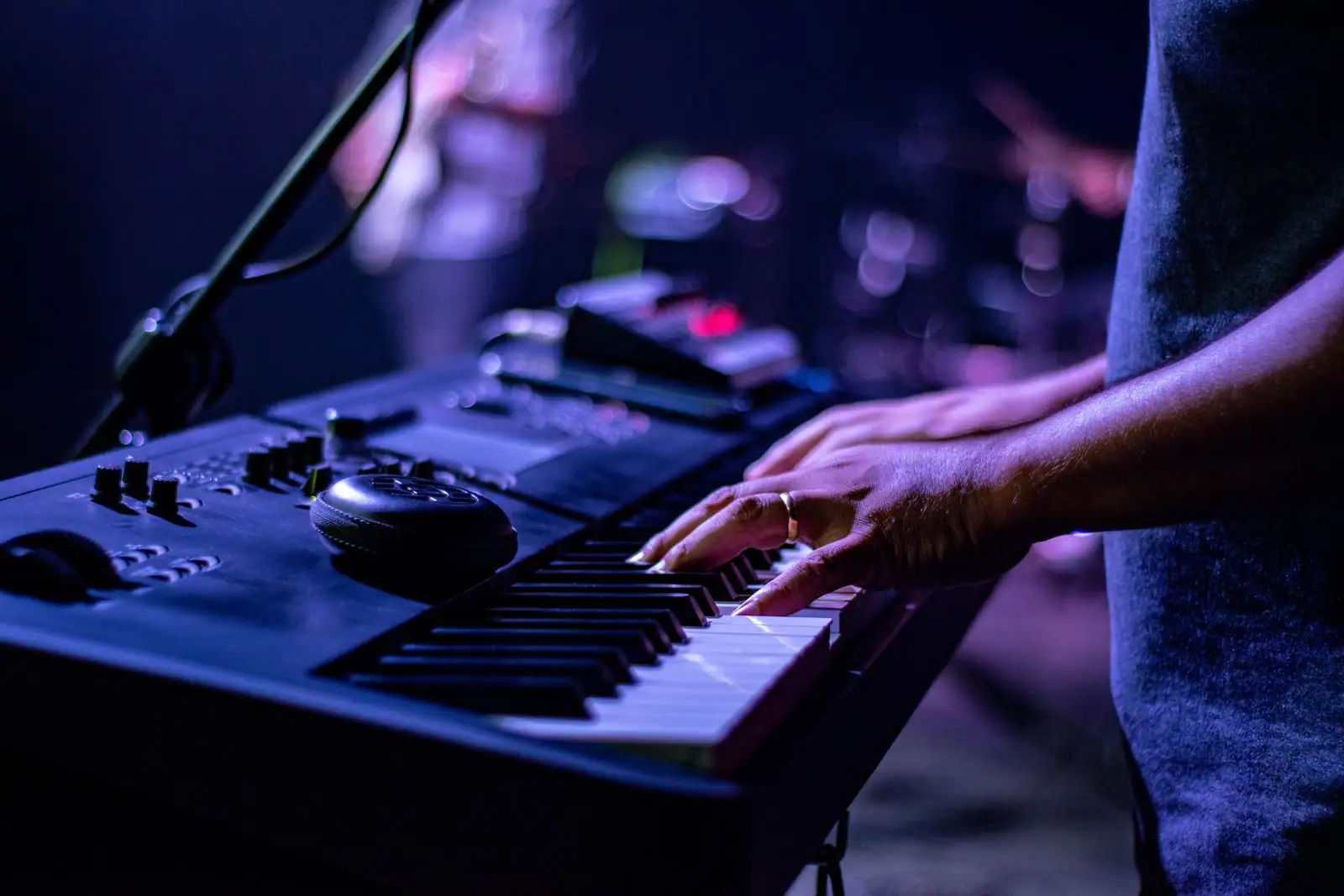 Mains d'un claviériste sur un synthétiseur de scène, sous les lumières bleutées d'un concert