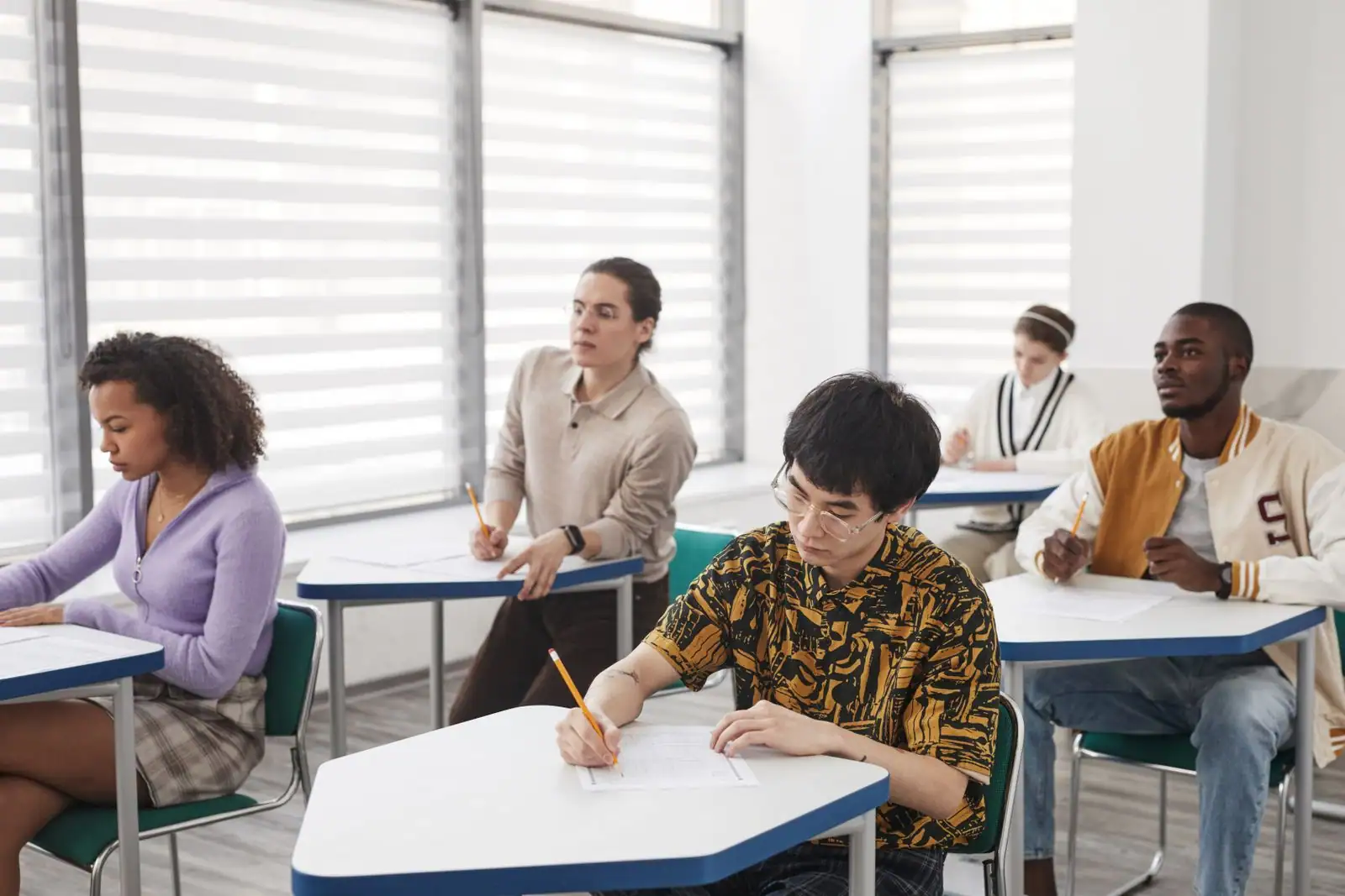 Candidats assis à des tables individuelles écrivant sur des feuilles pendant une épreuve écrite