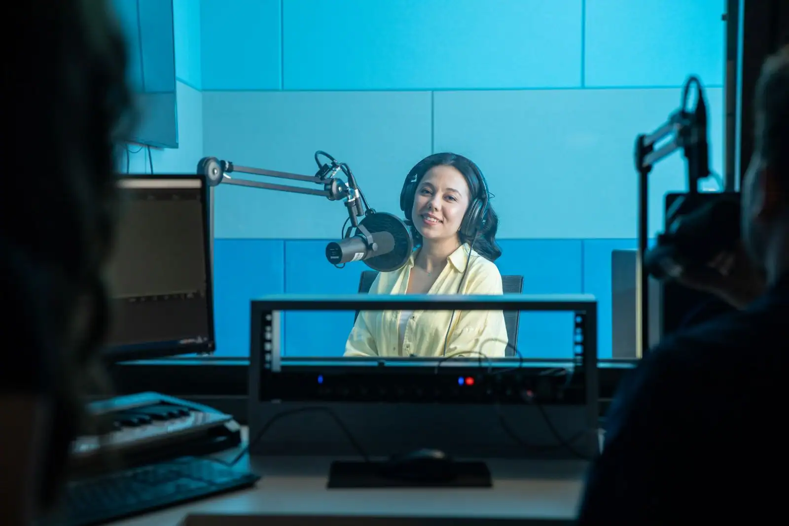 Animatrice au micro dans un studio de radio, casque sur les oreilles, écrans et panneaux acoustiques autour