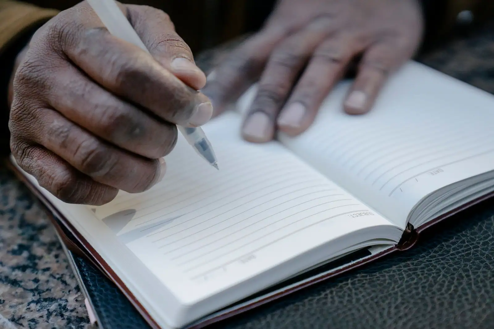 Gros plan sur les mains d'un adulte tenant un stylo au-dessus d'un carnet ligné resté vierge