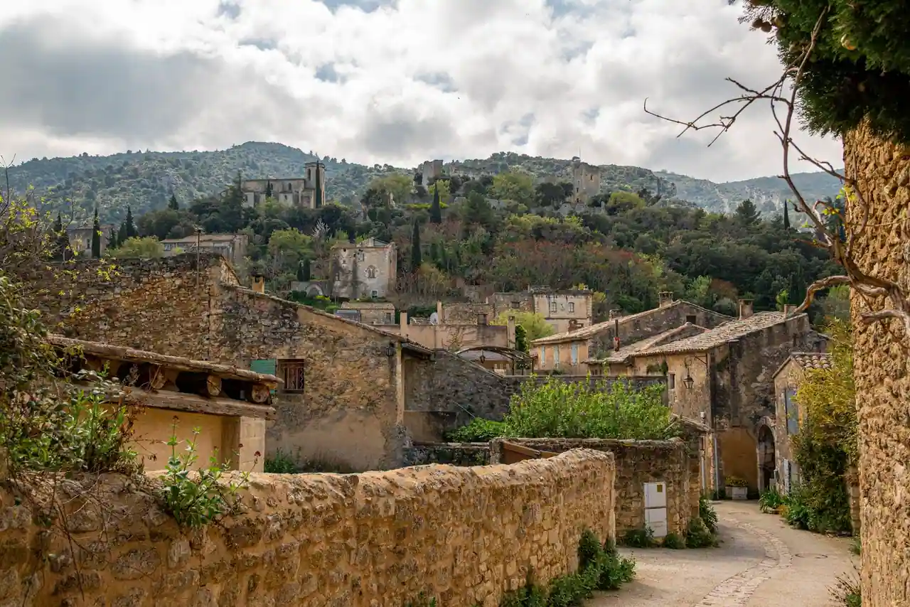 Village provençal en pierre adossé à une colline boisée, maisons anciennes et ruelle pavée