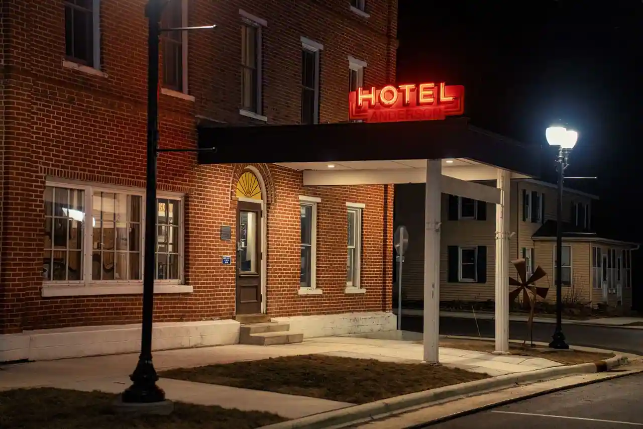 Enseigne lumineuse rouge d'un hôtel en brique, la nuit, au-dessus de son entrée sur rue.