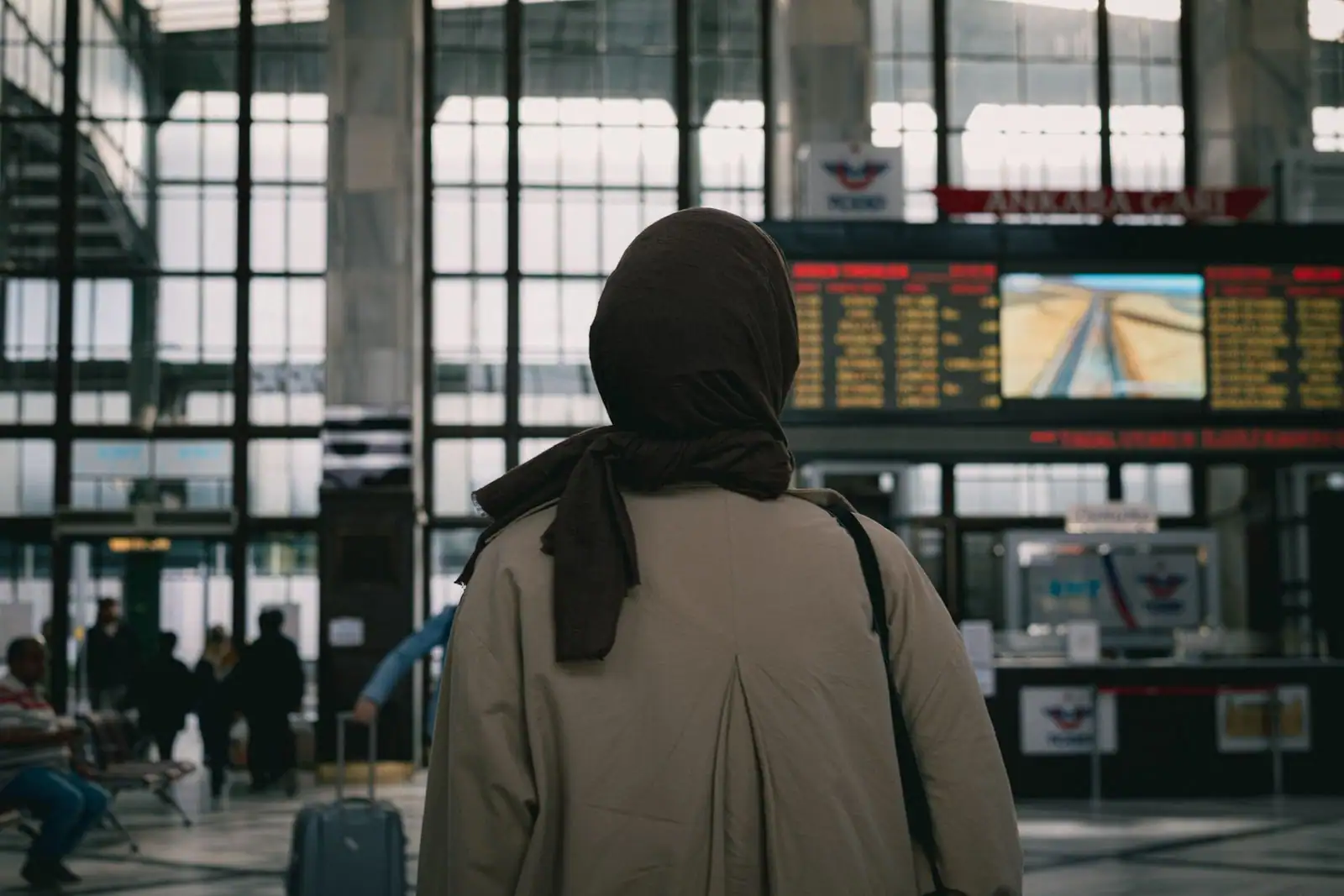Une personne de dos consulte les panneaux d'affichage des départs dans le hall d'une gare