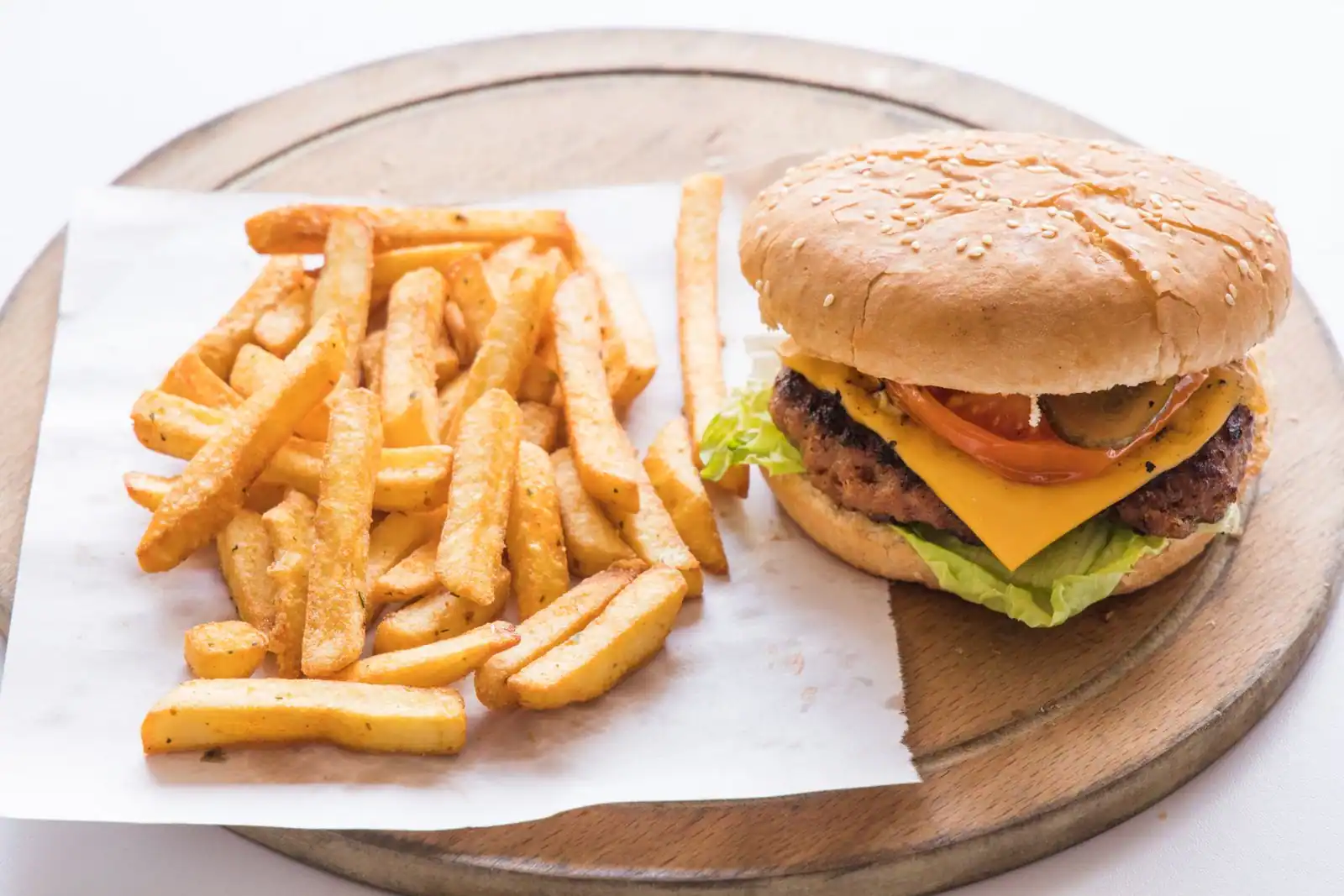 Un hamburger et une portion de frites présentés sur une feuille de papier, posée sur une planche en bois.