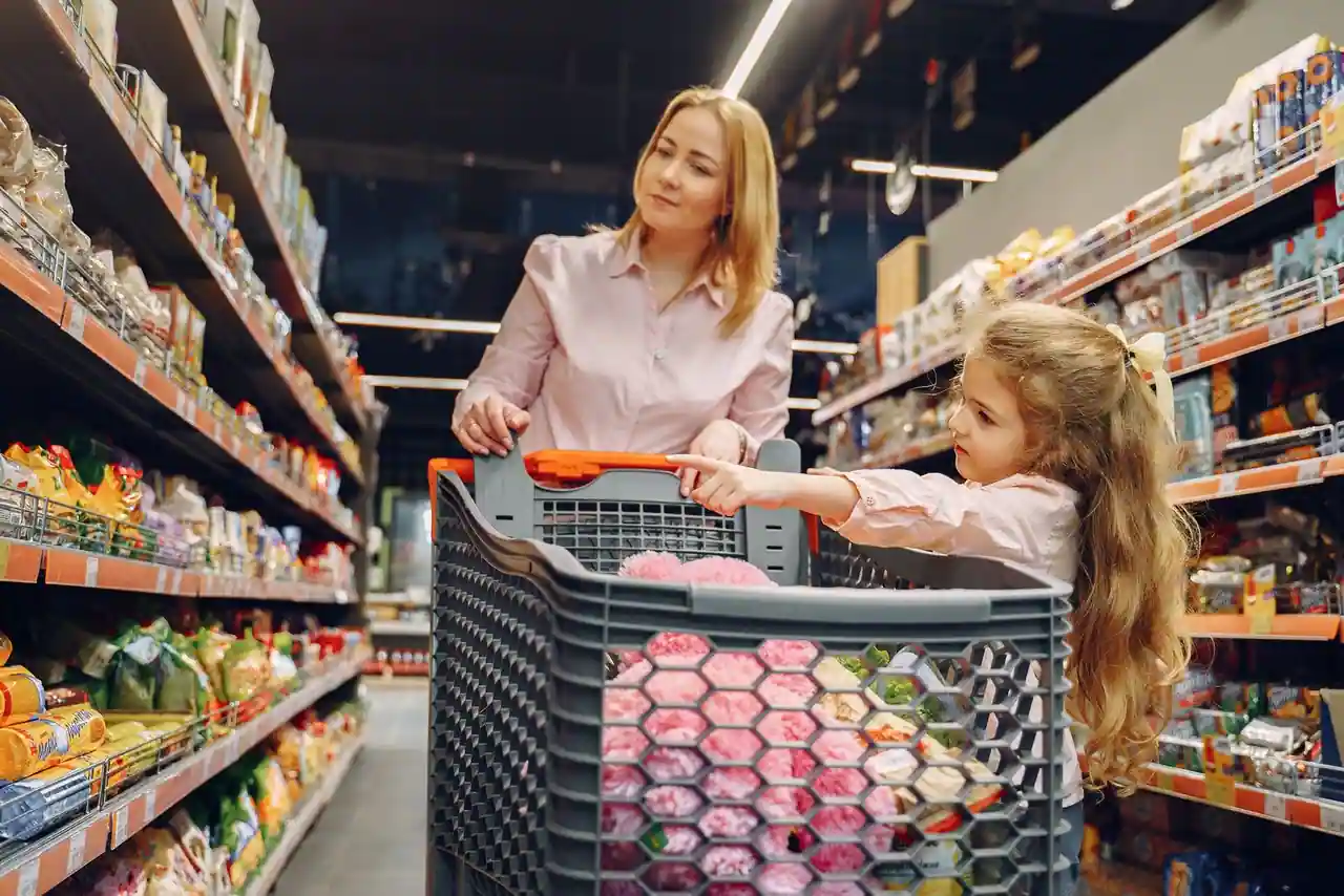 Une femme pousse un chariot de courses dans une allée de supermarché, une fillette assise dedans