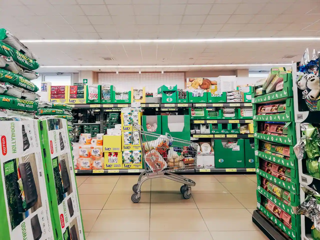 Chariot rempli de courses au milieu d'un rayon de supermarché bordé d'étiquettes jaunes