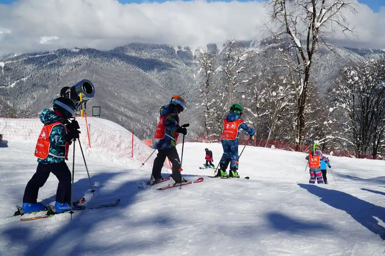 Groupe d'enfants casqués et en dossards de cours de ski sur une pente enneigée face aux montagnes