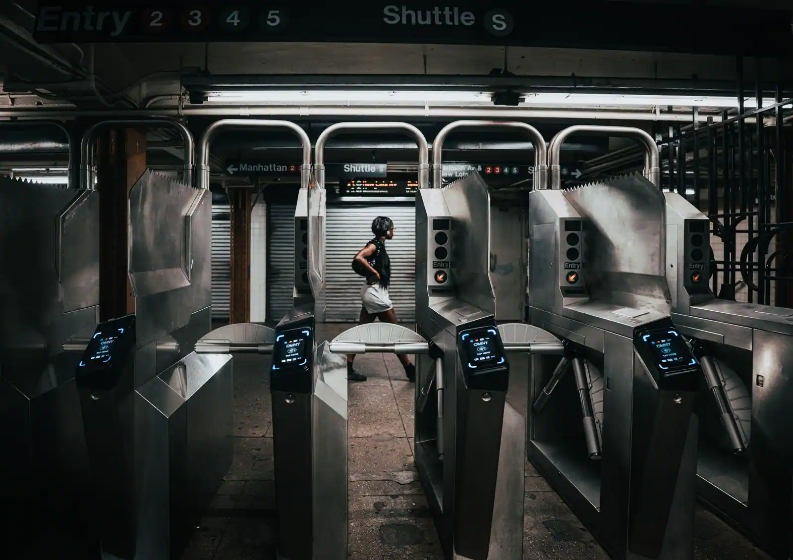 Tourniquets d'accès au métro de New York équipés de lecteurs sans contact, une passante à l'arrière-plan.