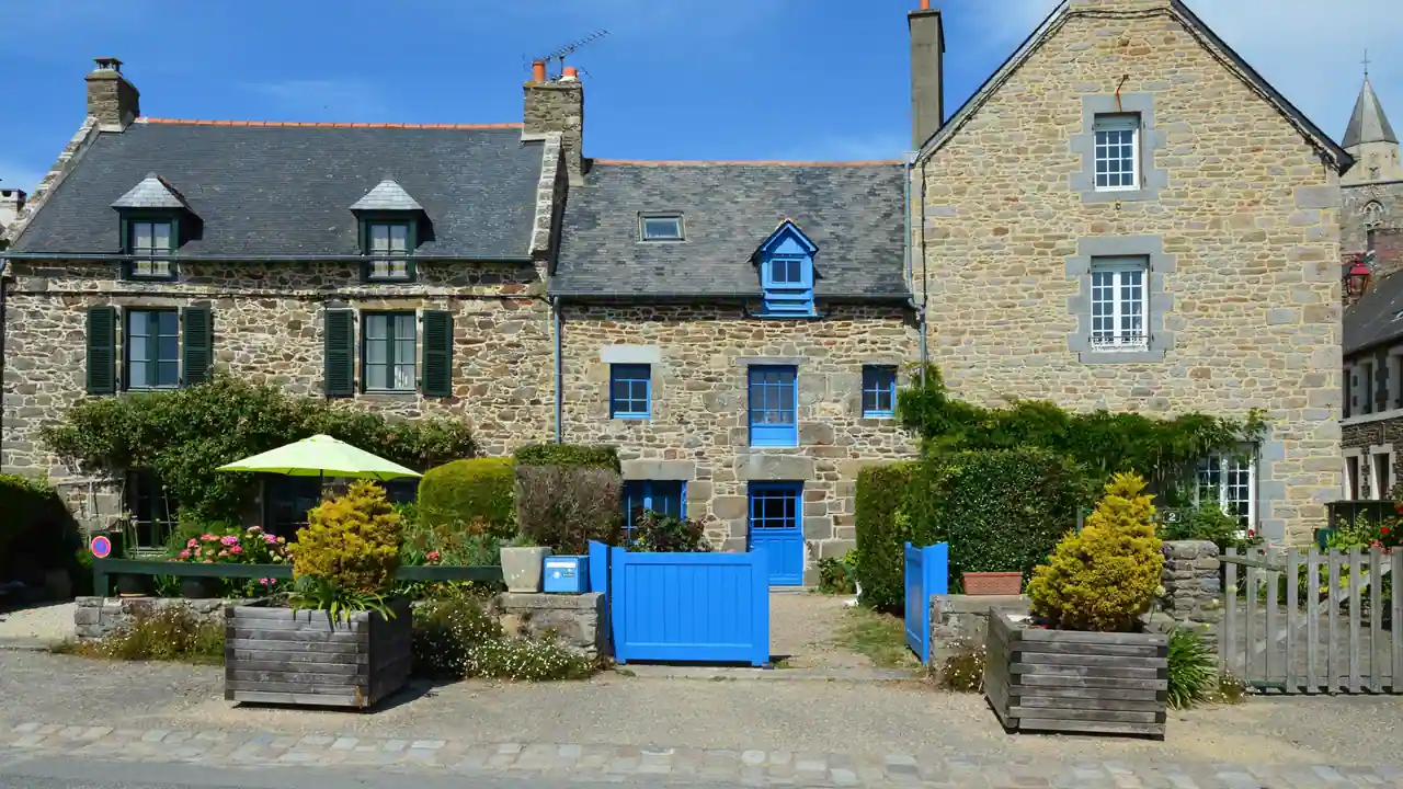 Maisons bretonnes en pierre à toit d'ardoise et volets bleus, sur une place de village ensoleillée