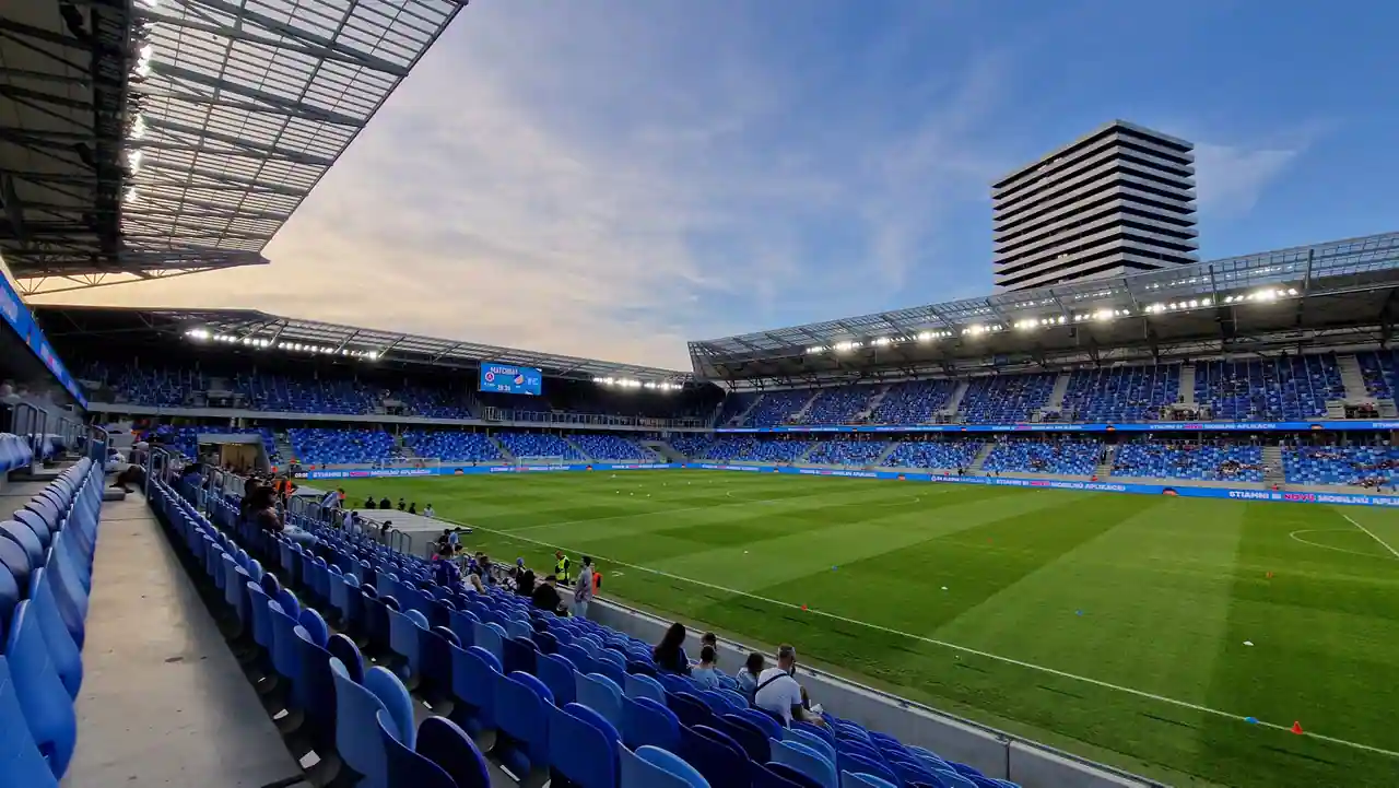 Tribunes d'un stade de football moderne qui se remplissent avant le coup d'envoi, en fin de journée