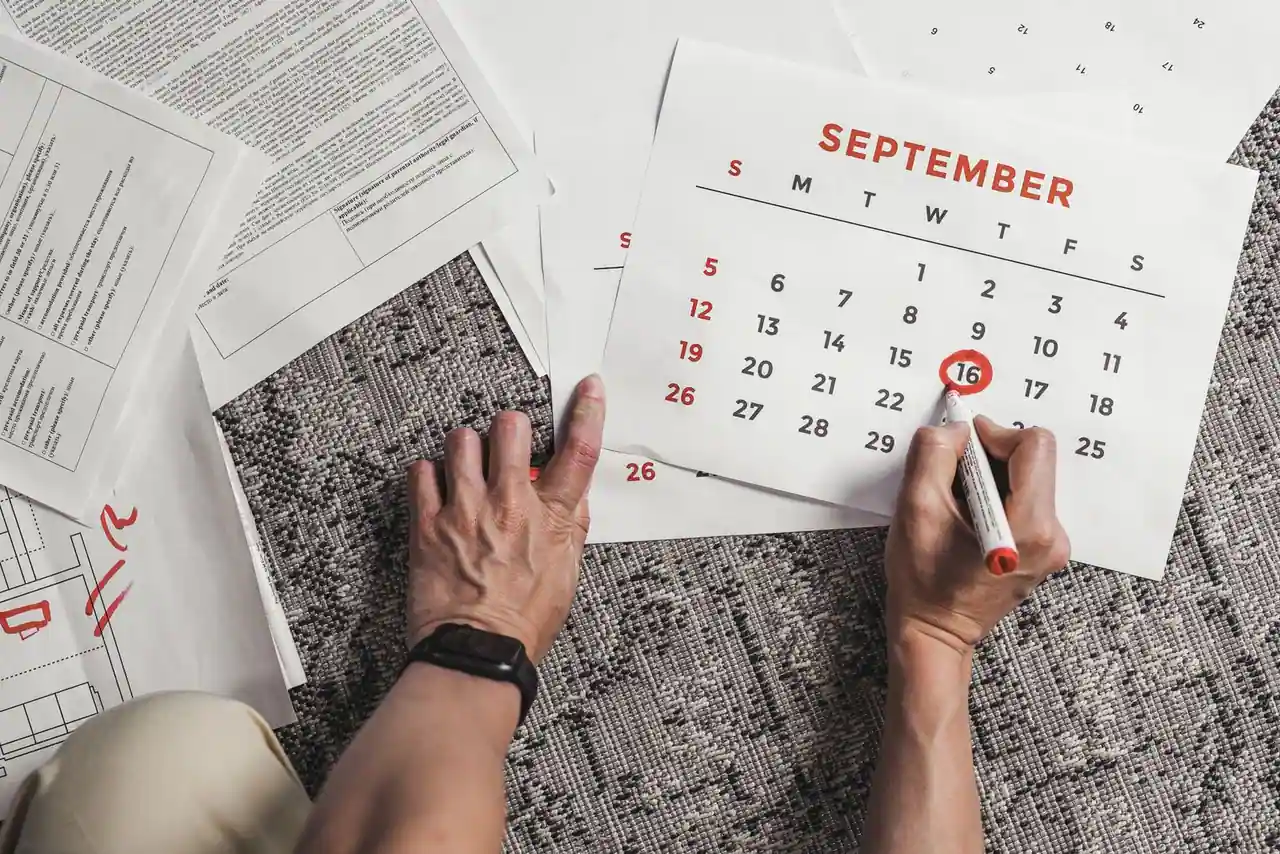 Mains entourant une date au feutre rouge sur un calendrier mensuel, parmi des documents imprimés.
