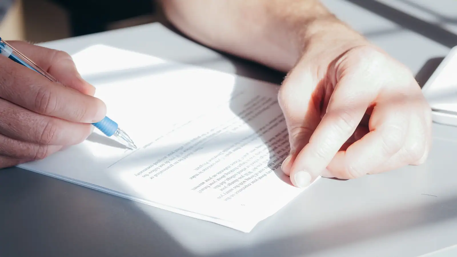 Un stylo à la main au-dessus d'un document imprimé, l'autre main tenant la page avant la signature