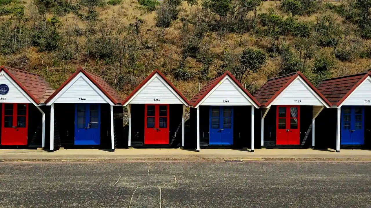 Rangée de cabines de plage anglaises numérotées, portes rouges et bleues, alignées le long d'une promenade