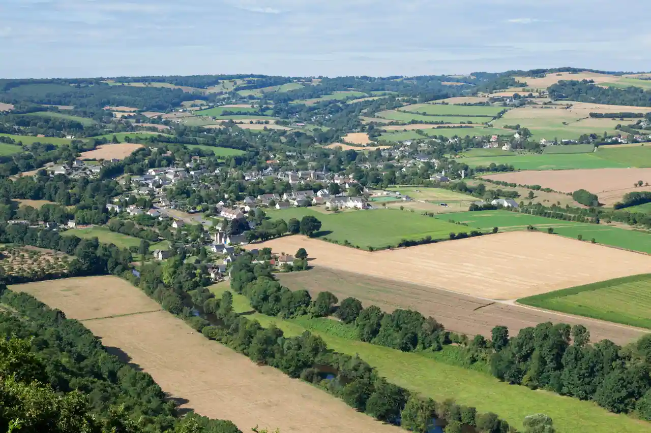 Vue plongeante sur un village normand, sa rivière et une mosaïque de champs jusqu'à l'horizon